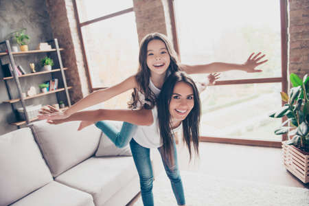 Cute playful joyful funny little girl is showing a plane on her mummy's back, she is piggy backの写真素材