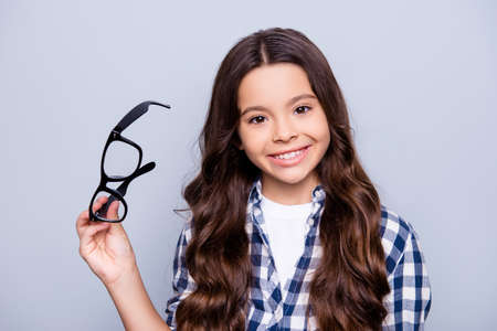 Close up portrait of beautiful, charming, little girl taking out glasses and using lenses, smiling to the camera standing over grey backgroundの写真素材