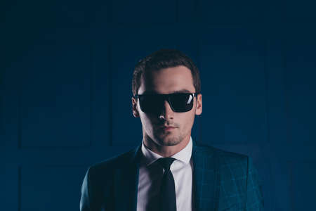 Close up portrait of trendy guard in checkered jacket, black glasses with serious expression over dark blue backgroundの写真素材