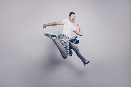 Happy young bearded attractive handsome man with opened mouth, jumping in air, triumphant, winner over grey backgroundの写真素材