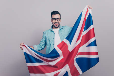 Portrait of attractive, handsome man in glasses and jeans shirt holding waving Jack Union flagの写真素材
