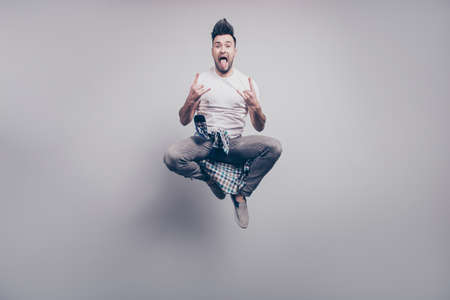 Happiness, freedom, motion and people concept. Crazy, bearded attractive handsome music lover jumping in air, gesturing rock and roll sign with hair up and tongue out over grey backgroundの写真素材