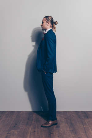 Full length side view portrait of man in formal wear outfit with  tail on his head, holding his hand in the pocket with serious expression over grey backgroundの写真素材