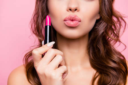 Close up cropped shot of femenine gorgeous charming adorable lady with amazing wavy hair do, tube of hard pink pomade in arm. Pampering, lips correction conceptの写真素材