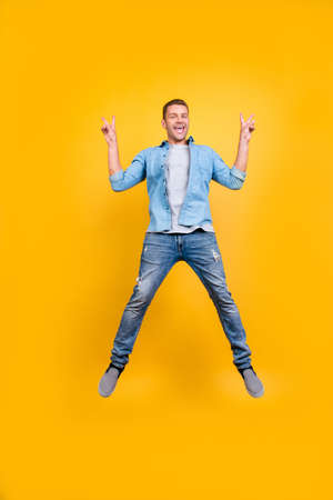 funky guy in casual outfit full of energy is jumping up, fooling, demonstrating v-sign with two hands, isolated over yellow backgroundの写真素材