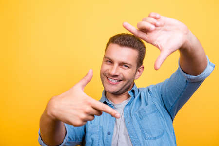 Closeup of young, happy man with stubble making diagonal frame in front of face with fingers, over...