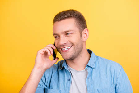 Close up portrait of bearded, cheerful, attractive man on holidays, weekend using smart phone to connect with friends and lover, talking with relatives, looking to the side over yellow backgroundの写真素材