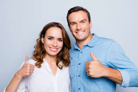 Closeup portrait of smiling couple gesturing thumbs up standing over grey backgroundの写真素材