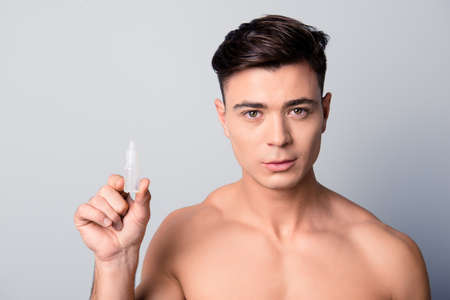 Close up portrait of confident handsome guy holding a bottle with artificial tears, isolated on grey backgroundの写真素材