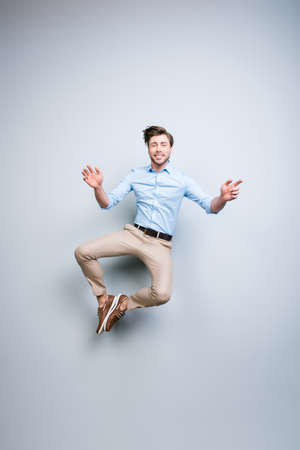 Happy, young, bearded, attractive handsome, smiling man in classic outfit  jumping in air putting his feet together over grey background