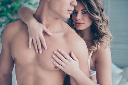 Cropped portrait of half face profile naked torso man and charming woman with hairstyle embracing his lover from back, holding hands on chest with serious expression looking at camera on valentine dayの写真素材