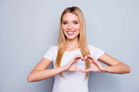 Portrait of happy smiling cheerful joyful attractive woman making a heart using her hands, isolated on grey backgroundの写真素材