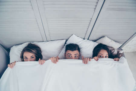 Top view of funny three partners hiding behind blanket, peeking over sheets and looking at camera...