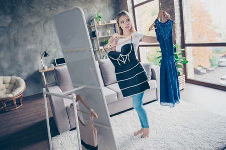 The first dress is wonderful and the second one is nice too! Beautiful attractive cute lovely unsure woman is holding dresses and doesn't know which one to chooseの写真素材