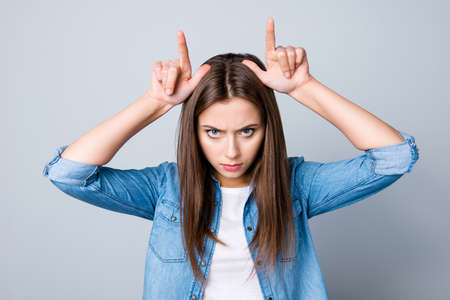 Close up portrait of devil concept of a nice girl  with raised hands holding two fingers as antlers...