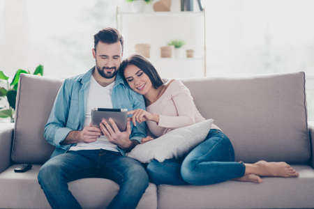 Pleased cheerful relaxed beautiful cute couple of lovers is buying ordering products on the internet and choosing furniture for their house using digital tablet cozy comfortable atmosphereの写真素材