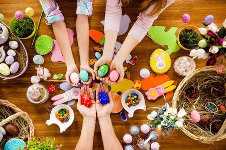 Top view horizontal photo of attractive beautiful colorful easter handmade objects subjects things baked cookies laying on wooden table and hands of family showing painted decorated small little eggsの写真素材