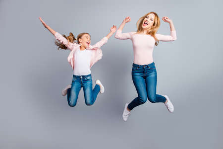 Cute, pretty, playful mother and daughter with open mouth jumping in the air over gray background, celebrating woman's day, yes, done, winners, victory, sisters screaming, shoutingの写真素材