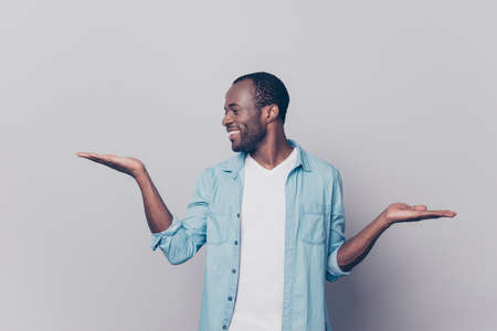 Portrait of cheerful excited satisfied man clothed in casual denim shirt and white t-shirt is showing a balance, looking on his hand, isolated on gray backgroundの写真素材