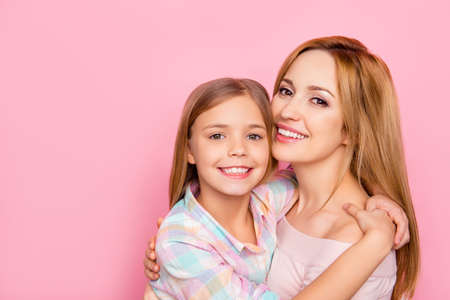 Close up portrait of pretty, charming mother and daughter with beaming smiles over pink background,...