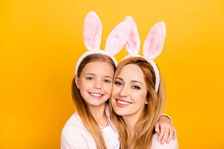 Close up portrait of charming cheerful excited carefree restless gentle tender nice amazing pure mom and small preteen school girl hugging cheek to cheek isolated on yellow backgroundの写真素材