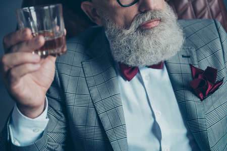 Close up cropped half face portrait of bearded old rich man in formal wear, sitting on armchair, holding glass with whiskey, shareholder, crypto-currency, shares, stockの写真素材