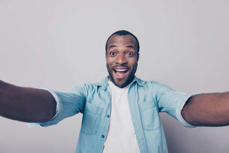 Hi guys! Portrait of adorable excited amazed funny joyful african man taking self portrait while having a trip around the world isolated on gray backgroundの写真素材