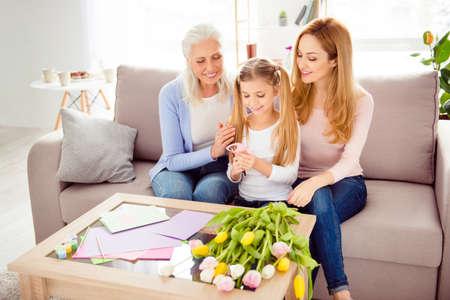 Rest comfort relax leisure creativity event spend time together concept. Cheerful sweet cute playful excited tender gentle schoolgirl cutting out 8 for postcard with granny mommy on divan living roomの写真素材