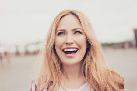 Close up portrait of delightful cheerful emotional optimistic careless beautiful  blonde laughing woman with beaming toothy smile, she is having a walk in a foreign cityの写真素材