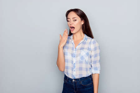 Portrait of tired, bored, nice, attractive woman in checkered shirt, closing her open mouth, she...