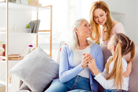 Parenthood tender gentle help aid maternity celebration comfort concept. Three cute cheerful excited sweet delightful beautiful mom mum mommy granny schoolgirl spending time together sitting on sofaの写真素材