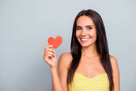 Concept of leading healthy lifestyle. Pretty beautiful attractive with toothy smile woman wearing dotted dress is showing red little head in hand, isolated on grey background, copy-spaceの写真素材