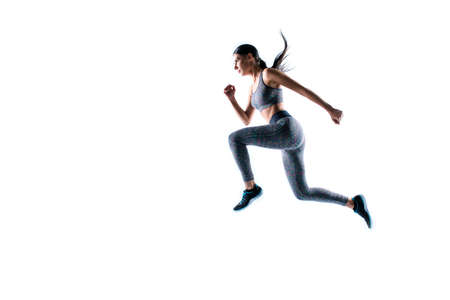 Dynamic movement. Full size side profile view portrait of strong sporty muscular beautiful running focused woman wearing tight sport clothing, isolated on white background, natural light, copy-spaceの写真素材
