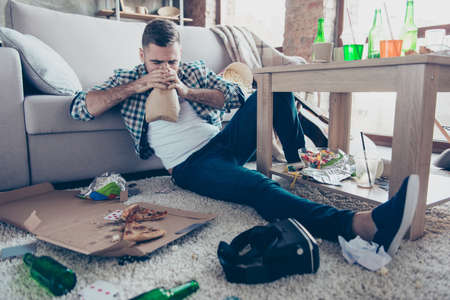 Drunk exhausted tired young man is suffering from nausea and panic attack, he is breathing in paper...