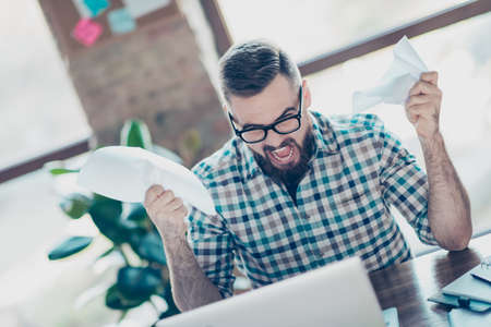 Depressed frustrated crazy freelancer dressed in checkered shirt and glasses is sitting at the...