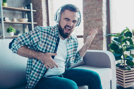 Attractive, bearded man sitting on the couch in living room, having headphones on his head,...