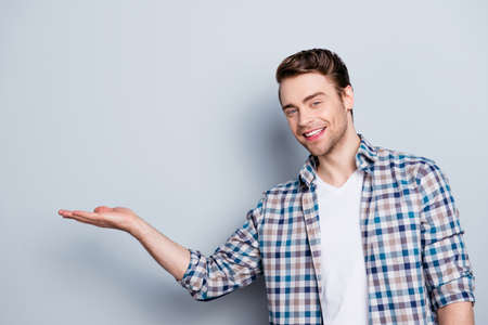 Close up portrait of successful, cheerful, cute, professional, young man presenting new product, start up, showing copy space on his palm, standing over grey backgroundの写真素材