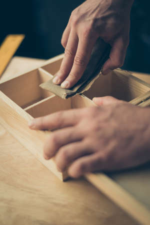 Close up cropped photo of carpenter's hands making smooth the surface on wooden casket using sandpaper he wants to sell his diyの写真素材