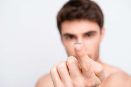 Attractive, handsome man over white blurred background with copy space showing focused contact lens on forefingerの写真素材