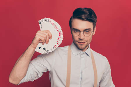 Professional, cunning magician, illusionist, gambler in casual outfit, glasses, holding, showing set deck of card near face, standing over red backgroundの写真素材