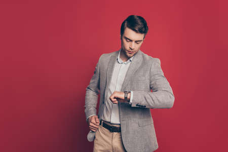 Portrait of punctual, virile, harsh, stunning financier looking at his watch on arm, nervous that his partner is late, isolated on red background, checking timeの写真素材