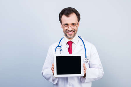 Portrait of experienced qualified cheerful confident doctor demonstrating blank empty black screen monitor of digital tablet wearing white with red tie formal-wearの写真素材