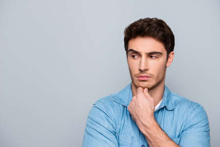 Portrait of harsh man in jeans shirt touching chin with arm, looking to the side, isolated on grey backgroundの写真素材