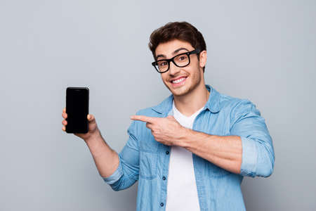 Portrait of cheerful, positive, attractive guy with stubble in jeans shirt, having smart phone with...