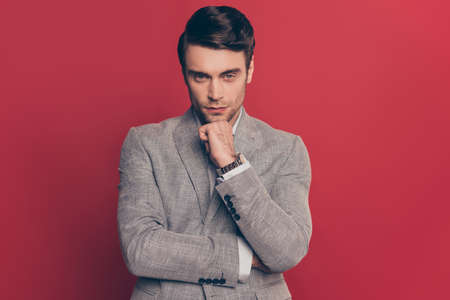 Portrait of manly, ponder, minded, strict, stunning man with stubble, holding arm with fist on chin, looking at camera, isolated on red backgroundの写真素材