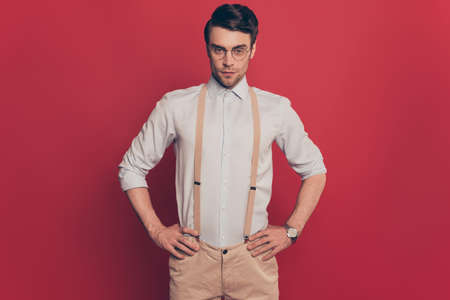 Portrait of virile, harsh modern fashion expert in glasses, holding two hands on waist, looking at camera, standing over red backgroundの写真素材