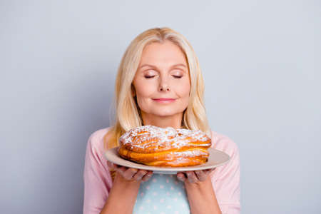 Close up portrait of peaceful calm satisfied cute lovely romantic with modern hairstyle granny smelling fresh tasty cake isolated on gray backgroundの写真素材