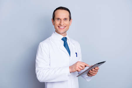 Portrait of cheerful glad gifted smart with toothy smile doctor using modern pad at work isolated on gray background copy-spaceの写真素材