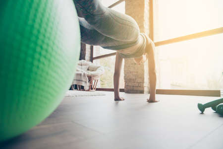 Behind bottom low-angle cropped closeup view photo of muscular slim beautiful woman wearing tight sportive leggings and top standing on hands doing push-ups, view on windowの写真素材