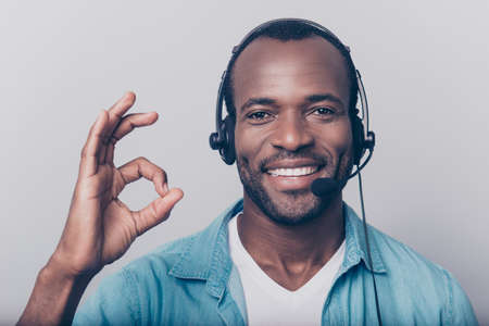 Close up portrait of attractive, joyful, cheerful, confident man in jeans shirt with bristle guy having using headset on head looking at camera showing ok sign, isolated on grey backgroundの写真素材
